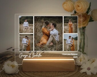 May include: A rectangular acrylic photo display featuring five printed photographs of a couple in a field. The base is made of light-colored wood with an integrated light. The text "George & Isabella" and "I love you forever 2025" is printed on the acrylic.