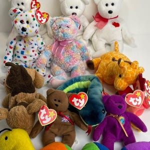 Puede incluir: Una colección de peluches Ty Beanie Babies de colores, que incluye un oso blanco con un corazón rojo, un oso multicolor, un oso marrón con una etiqueta de la Union Jack, un oso morado con una etiqueta azul, una jirafa amarilla y naranja, un perro marrón y blanco, una serpiente verde y una oruga amarilla y arcoíris.