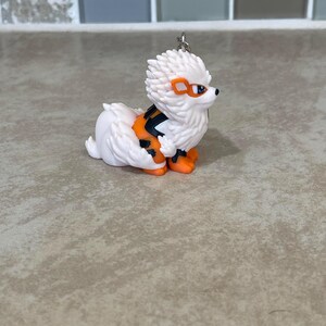 May include: A white and orange figurine of a dog-like creature with a spiky head, orange accents, and black stripes. The figurine has orange feet and a small silver keychain loop.