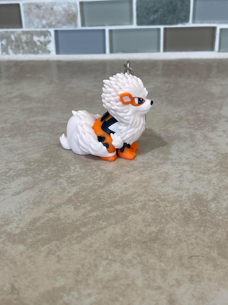 May include: A white and orange figurine of a dog-like creature with a spiky head, orange accents, and black stripes. The figurine has orange feet and a small silver keychain loop.