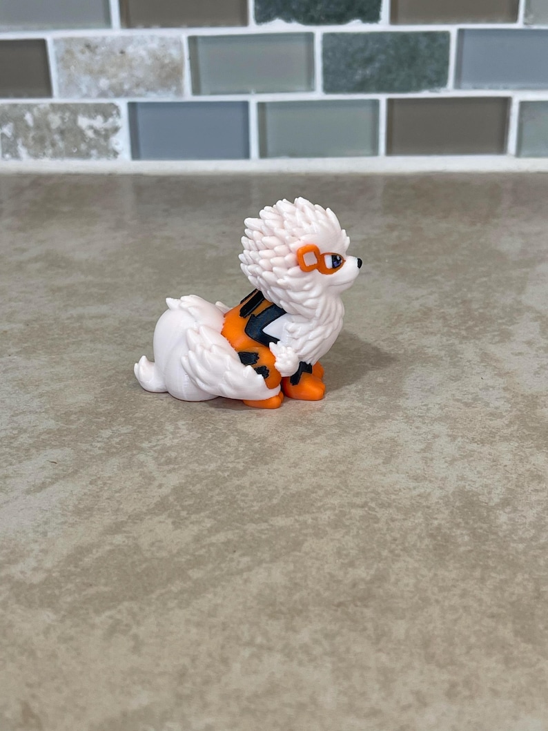 May include: A white and orange figurine of a dog-like creature with spiky fur and orange accents. The figurine has orange goggles and black and orange markings on its back. The creature is in a sitting position.