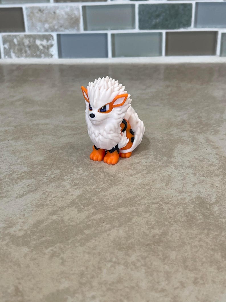 May include: A small, white and orange figurine of a creature with a spiky mane, orange accents, and a black and orange striped pattern on its back. The figurine has orange paws and a determined expression.