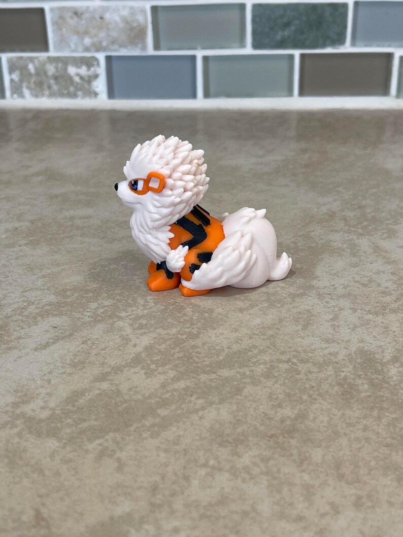 May include: A white and orange figurine of a dog-like creature with a spiky mane, orange accents, and black stripes. The figurine has orange feet and a small tail. The creature has orange goggles and a black nose.