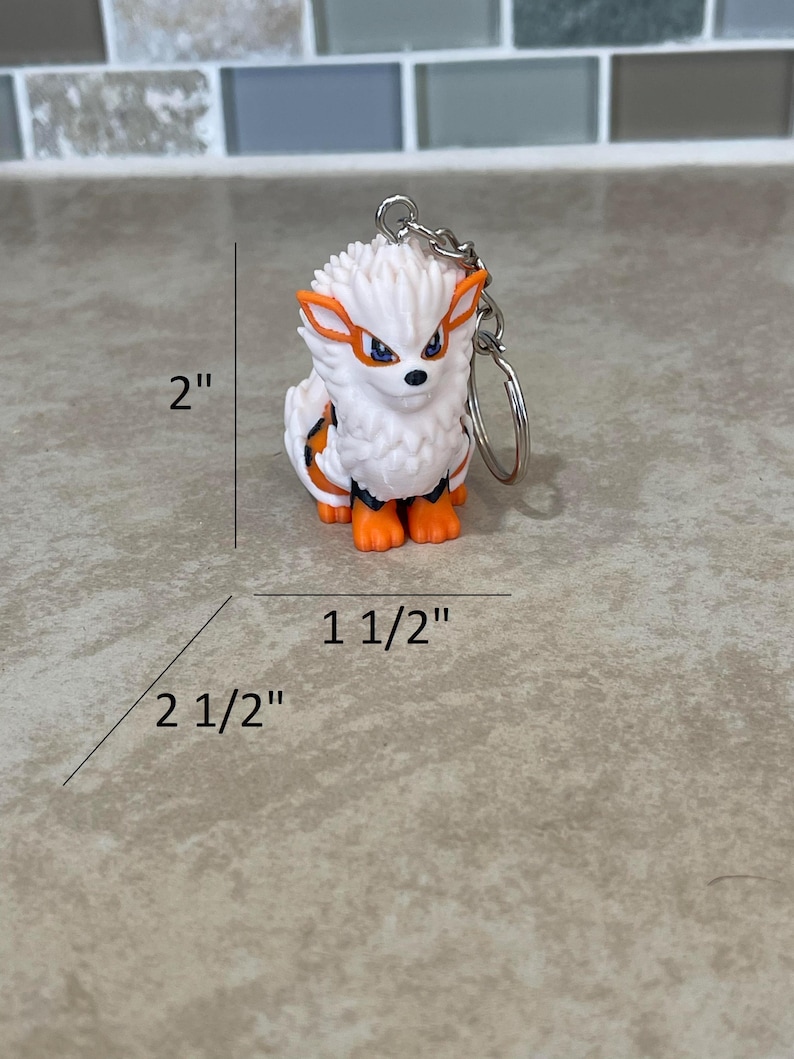 May include: A white and orange Arcanine keychain, measuring approximately 2 inches tall, 2.5 inches long, and 1.5 inches wide. The keychain features a detailed design of the Pok&eacute;mon character with a silver chain and keyring.