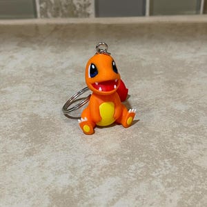 May include: Orange and yellow Pokemon keychain featuring a cartoon character with a red mouth and blue eyes.