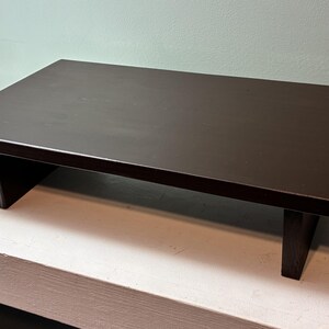 May include: A dark brown, rectangular wooden table with a low profile. The table is 24 inches long, 12 inches wide, and 4 inches high, with two rectangular legs. The table is suitable for various uses.