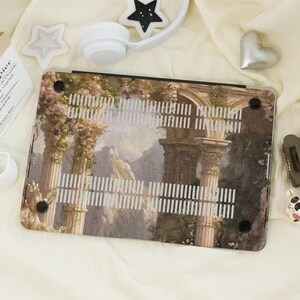 May include: A laptop case featuring a classical landscape design with columns, arches, and mountains in the background. The case has a light color palette with hints of pink and green, and a series of vertical cutouts.