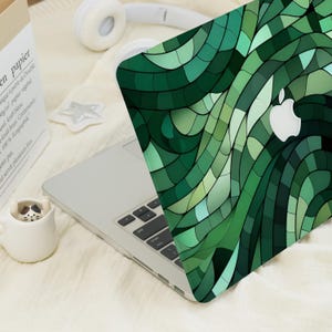Peut inclure: Coque d'ordinateur portable avec un motif de mosaïque verte et un logo Apple blanc. Le motif est composé de différentes nuances de vert, créant un motif géométrique abstrait. L'ordinateur portable est ouvert, révélant le clavier.