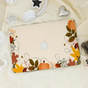 May include: A cream-colored laptop skin featuring a decorative border of orange pumpkins, yellow and brown autumn leaves, small flowers, and tiny bees. The design includes thin black swirling lines connecting the botanical elements around the center.
