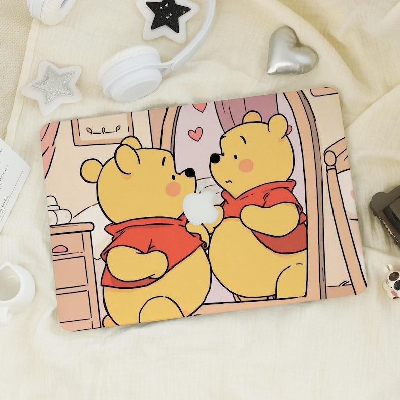 May include: A rectangular laptop case with a cartoon illustration of Winnie the Pooh and a friend. The characters are yellow with red shirts, set against a soft pink and beige background. The case has a smooth finish.