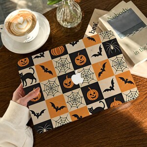 Può includere: Una skin per laptop con un motivo a scacchi composto da quadrati arancioni, neri e color crema. Il design presenta illustrazioni di zucche, gatti neri, ragnatele e pipistrelli applicata su un laptop con il logo Apple visibile.