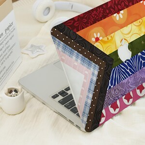 May include: A laptop skin featuring a vibrant, multi-colored diagonal striped pattern. The design includes sections with floral motifs, polka dots, plaid, and star shapes in shades of red, orange, yellow, green, blue, purple, and pink.