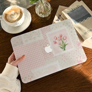 Op de afbeelding: Een laptophoes met een patchworkontwerp van zachtroze en witte patronen, waaronder vichy, kleine bloemenprints en een centrale rechthoekige afbeelding van een boeket roze tulpen. De hoes heeft een uitsparing voor het Apple-logo in het midden.