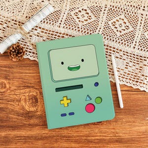 May include: A teal tablet case featuring a cartoon face with a smiling mouth and a rectangular screen. The case has a yellow plus sign, a pink circle, and blue and green shapes. A white stylus is next to the case.