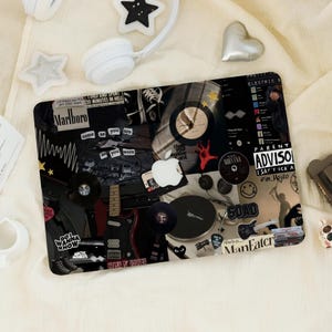 Peut inclure: Peau d'ordinateur portable noire avec un collage d'images comprenant une guitare, un tourne-disque, un paquet de cigarettes et une cassette. Le texte "Marlboro", "come as you are", "I hold your explosive hand", "Nirvana", "SOAD", "Parent Advisory", "I say f*** a eim Mojito", et "She's a... ManFater" est visible sur la peau.