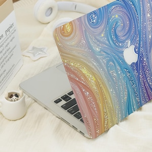 May include: A laptop with a protective cover featuring a swirling, abstract pattern of blue, purple, yellow, and orange hues with white speckles. The cover displays a cutout for the Apple logo, and the laptop is open to reveal a silver keyboard.