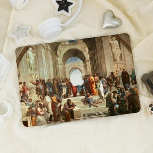 May include: A rectangular laptop skin displaying a Renaissance painting with many figures in classical dress. The artwork uses warm colours like red, orange, and brown, with architectural details in the background. The Apple logo is visible.