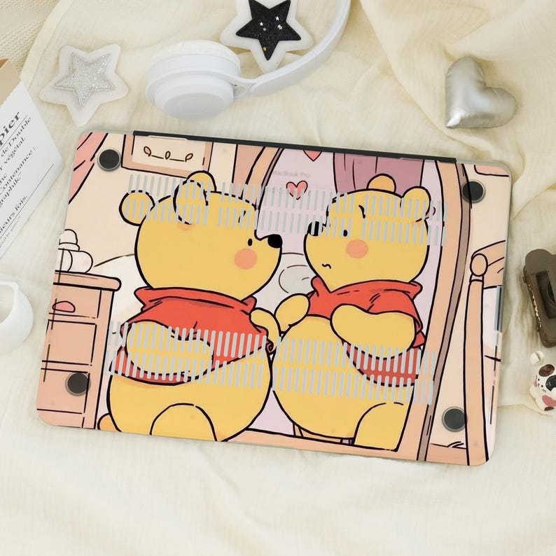 May include: A laptop case with a cartoon illustration of Winnie the Pooh looking in a mirror. The case has a light beige background with a bedroom scene. The cartoon character is yellow with a red shirt.