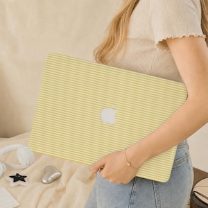 May include: A laptop skin featuring a pattern of thin, horizontal yellow and white stripes. The skin is applied to the exterior of a laptop, with the silver Apple logo visible in the centre of the striped design, creating a clean and uniform look.