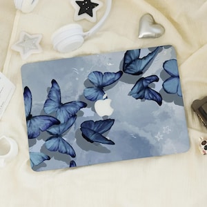 May include: A laptop case with a design of blue butterflies on a light blue background. The butterflies have detailed wing patterns and are scattered across the surface. The Apple logo is visible in the centre.