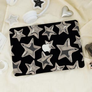 Op de afbeelding: Zwarte laptophoes met een patroon van zilveren metallic sterren. De hoes heeft een glanzende afwerking en een wit Apple-logo. De sterren zijn gelijkmatig verdeeld.