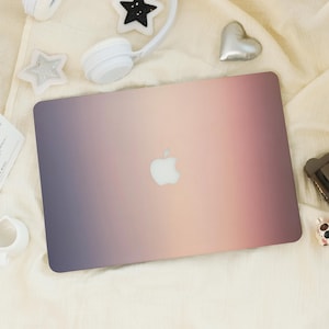 May include: A laptop with a gradient design in shades of purple, pink, and peach. The Apple logo is centered on the lid. The laptop is surrounded by white accessories, including headphones and star-shaped decorations.