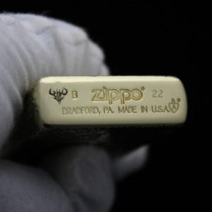 May include: Close-up of a gold Zippo lighter with a detailed engraving. The bottom of the lighter has the text "Zippo", "Bradford, PA Made in USA", and the number "22".