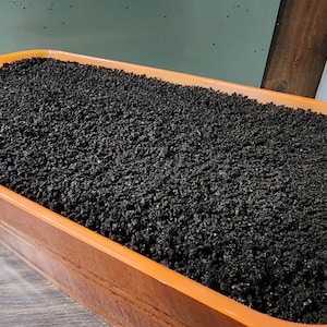 May include: A close-up of a terracotta-colored rectangular planter filled with dark brown compost.
