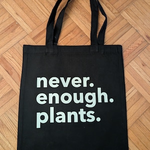 May include: Black canvas tote bag with white text that reads "never. enough. plants."
