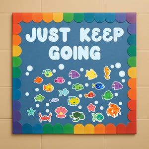 May include: A square, blue decorative board with the words "JUST KEEP GOING" in white. The board is decorated with colorful fish and sea creatures. The border is a rainbow of colors.