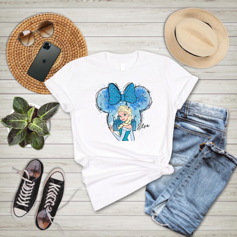 May include: White t-shirt with a blue and white watercolor design of a Disney princess with a bow and the text "Elsa".