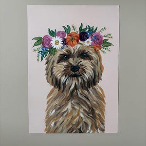 May include: A dog portrait with a floral crown. The artwork features a brown and tan dog with a fluffy coat, centered on a light pink background. The crown is composed of purple, orange, and white flowers with green leaves.