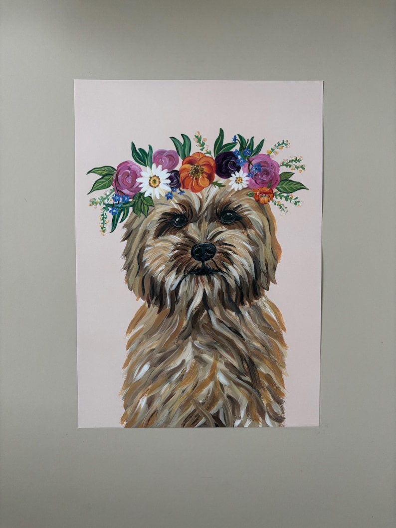 May include: A dog portrait with a floral crown. The artwork features a brown and tan dog with a fluffy coat, centered on a light pink background. The crown is composed of purple, orange, and white flowers with green leaves.