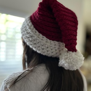 Könnte beinhalten: Eine rot-weiße gehäkelte Weihnachtsmütze mit einem weißen Bommel am Ende der Mütze.