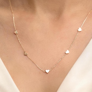 May include: A delicate gold necklace with small heart pendants. The necklace has a fine chain and multiple heart charms evenly spaced along its length. The hearts are a warm gold colour, creating a simple yet elegant design.