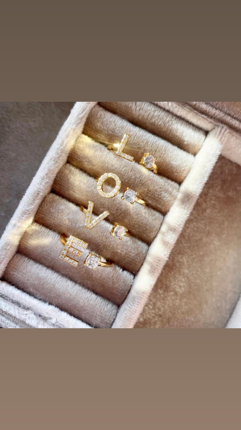 May include: A set of four gold rings with clear stones spelling out the word "LOVE". The rings are displayed in a velvet ring box.