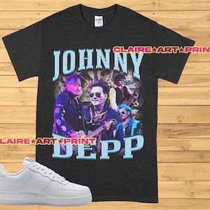 Könnte beinhalten: Schwarzes T-Shirt mit einem Grafikdruck von Johnny Depp und dem Text "JOHNNY DEPP" in Blau und Weiß. Die Grafik zeigt Depp in einer Band mit anderen Musikern. Das T-Shirt liegt auf einer Holzoberfläche mit einem weißen Sneaker.