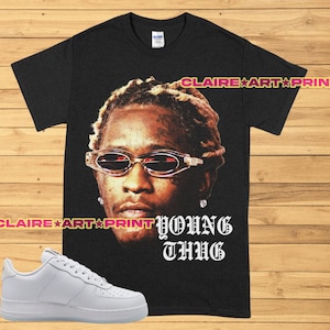May include: Black t-shirt featuring a graphic of Young Thug wearing sunglasses. The text "YOUNG THUG" is printed in white below the image.
