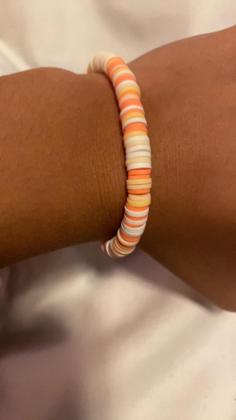 Peut inclure: Un bracelet color&eacute; compos&eacute; de perles rondes en plastique empil&eacute;es dans des tons de blanc, p&ecirc;che et orange.