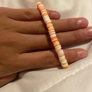 Peut inclure: Un bracelet color&eacute; compos&eacute; de petites perles rondes dans des tons d'orange, de blanc et de jaune.