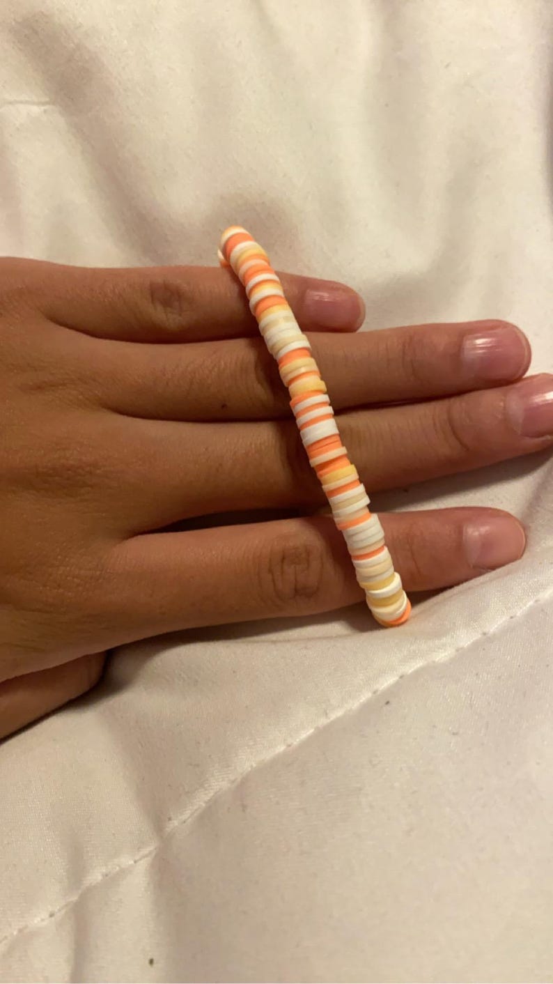 Peut inclure: Un bracelet color&eacute; compos&eacute; de petites perles rondes dans des tons d'orange, de blanc et de jaune.