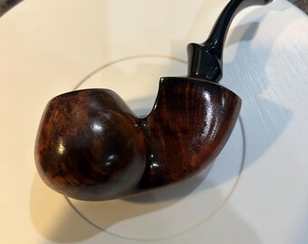 May include: A brown wooden smoking pipe with a black mouthpiece. The pipe has a rounded bowl and a curved stem.