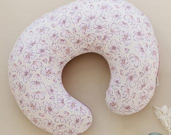 Peut inclure: Un coussin d'allaitement imprimé de fleurs blanches et roses avec une bordure rose. Le coussin est en forme de croissant de lune et est conçu pour soutenir une femme enceinte ou une nouvelle mère pendant l'allaitement.