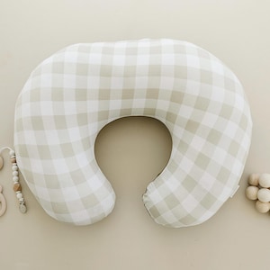 May include: A beige and white gingham nursing pillow. The pillow is shaped like a crescent moon and has a hole in the middle for the baby's head.