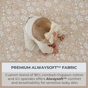 Peut inclure: Un b&eacute;b&eacute; en tenue cr&egrave;me et bandeau &agrave; n&oelig;ud papillon est allong&eacute; sur un tissu beige &agrave; motifs floraux blancs. Le tissu pr&eacute;sente un motif r&eacute;p&eacute;t&eacute; de fleurs et de feuilles blanches. Le texte en bas indique "PREMIUM ALWAYSOFT&trade; FABRIC".