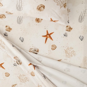 May include: White bedding with a beige and brown seashell and starfish pattern. The fabric has a subtle speckled texture.