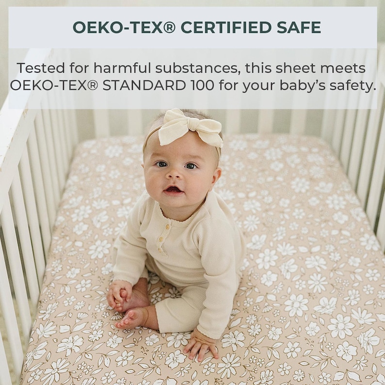 Peut inclure: Un b&eacute;b&eacute; est assis dans un lit b&eacute;b&eacute; sur un drap &agrave; motifs floraux. Le drap est beige avec des fleurs blanches. Le b&eacute;b&eacute; porte une tenue beige et un bandeau avec un n&oelig;ud. Le texte en haut indique "OEKO-TEX&reg; CERTIFIED SAFE".