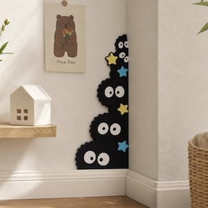 May include: Black, cartoon-like wall decor featuring multiple round, fluffy shapes with large white eyes. Yellow and blue star accents are interspersed among the shapes. A small house and a bear illustration with the text "Nice Day" are also visible.