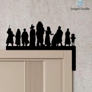 May include: Black metal silhouette of a group of figures, possibly from a fantasy series, mounted on a door frame. The figures include a wizard, a child, and a large, furry character. The design is a decorative accent for a door or wall.
