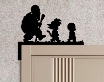 May include: Black metal silhouette of three figures walking on a ledge, suitable for door or wall decoration. The characters are an older man with a staff, a young boy with spiky hair, and a small child. The design is mounted on a door frame.